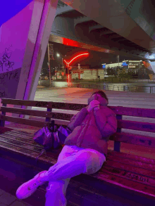 a person sitting on a bench under a bridge with graffiti on the wall that says ' a ' on it