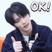 a young man in a denim jacket is giving a thumbs up and the word ok is above him .