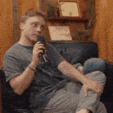 a young man is sitting in a chair holding a microphone and wearing a t-shirt with the letter t on the front
