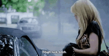 a woman is standing next to a car and says `` tough luck , bitch '' .