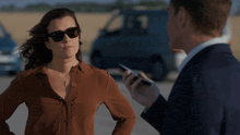a woman wearing sunglasses is standing next to a man holding a cell phone