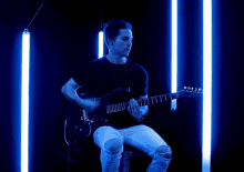 a man playing a guitar in a dark room with blue lights behind him