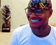 a man wearing glasses and a bandana smiles in front of a book shelf