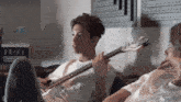 a man sits on a couch playing a guitar while another man looks on