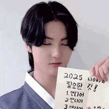 a young man in a kimono is holding a piece of paper that says 2025 in korean .