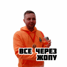 a man wearing an orange hoodie is holding a glass of wine and a medal around his neck that says " все через жопу "