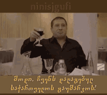 a man is holding a glass of wine in front of a sign that says ninisjgufi