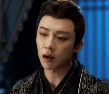 a young man in a traditional costume with a crown on his head is making a funny face .