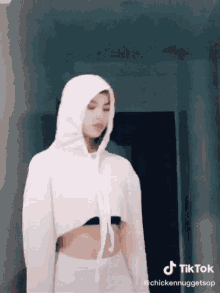 a woman wearing a white crop top and a white hoodie has a tik tok watermark