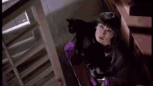 a woman in a purple jacket is holding a black cat in her lap .