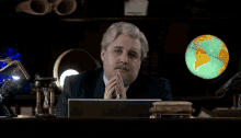 a man sitting at a desk with a globe in the background