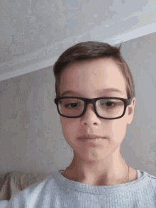 a young boy wearing glasses and a grey shirt looks down at the camera