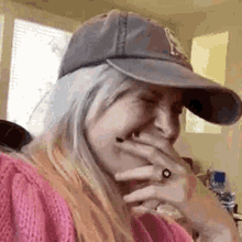 a woman wearing a baseball cap and a ring is laughing .