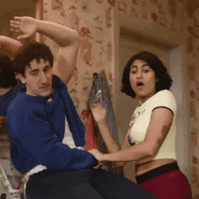 a man in a blue sweater and a woman in a crop top are dancing together
