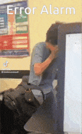 a man covering his face in front of a computer screen with error alarm written on the top