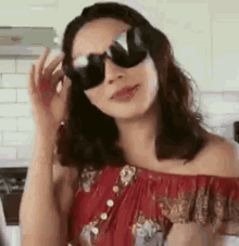 a woman wearing sunglasses is standing in a kitchen .