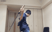 a man in a blue shirt is holding a large sword in a room with a honeycam watermark on the bottom right