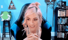 a woman with pink hair is sitting in a blue chair and smiling