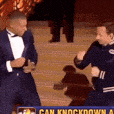 two men are dancing in front of a sign that says can knock down a