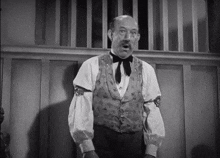 a man in a vest and bow tie is standing in front of a wall .