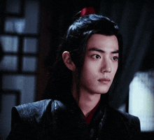 a young man with long black hair and a red ponytail is looking at the camera .