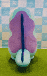 a purple and blue stuffed animal is sitting on a green carpet