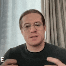 a man wearing glasses and a black shirt has the letter e on the bottom right