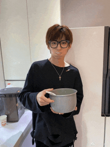 a man wearing glasses and a necklace holds a pot