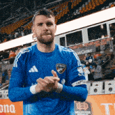 a man wearing a blue fc dallas jersey is clapping