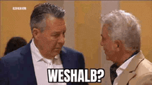 two men in suits are talking to each other and one of them is asking the other , weshall ?