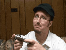 a man wearing glasses and a hat holds a video game controller