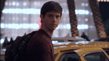 a man with a backpack stands in front of a yellow taxi cab