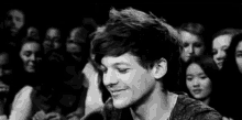a black and white photo of a man smiling in front of a crowd .
