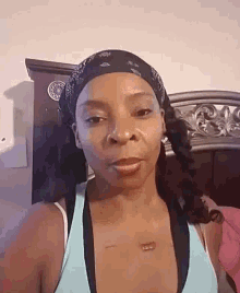 a woman wearing a bandana and a blue tank top looks at the camera .
