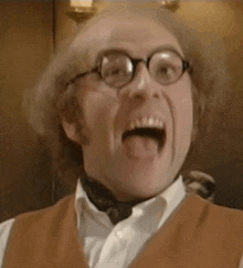 a man wearing glasses and a vest is making a funny face with his tongue out .