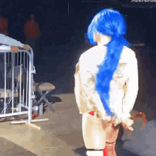 a woman in a blue wig is standing in front of a fence .