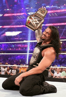 roman reigns is kneeling down in a wrestling ring holding a wwe world heavyweight championship belt