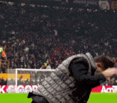 a man in a vest is dancing on a soccer field with a crowd in the background and a sign that says acigol