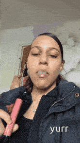 a woman in a black jacket is smoking a pink e-cigarette