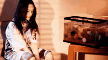 a woman sits in front of a small fish tank with stuffed animals in it