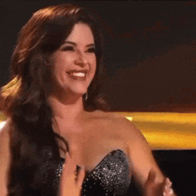 a woman in a strapless dress is clapping her hands while smiling .