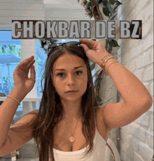 a woman adjusts her sunglasses with a chokbar de bz sign behind her