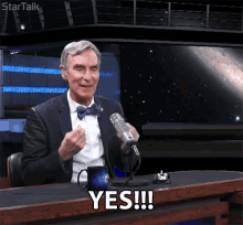 a man in a suit and bow tie is sitting in front of a microphone and says yes