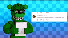 a green teddy bear is holding a piece of paper in his hands .