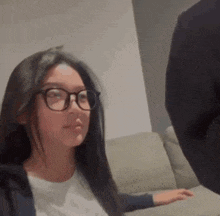 a woman wearing glasses is sitting on a couch looking at a man .