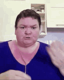 a woman in a blue sweater is making a funny face and waving her hands in a kitchen .