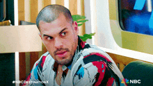 a man in a colorful shirt is sitting in front of a sign that says nbc destination x