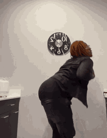 a woman stands in front of a clock that shows the time as 10:12