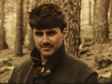 a man with a mustache in the woods looks at the camera