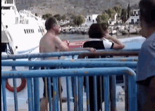 a man without a shirt is standing next to a woman on a boat behind a fence .
